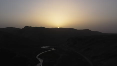 Epic-sun-setting-over-a-mountain-range-in-Kyrgyzstan,-drone-shooting-into-the-sun