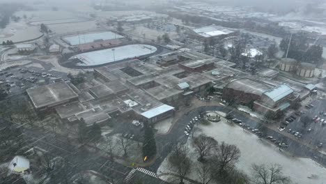 High-aerial-orbit-around-large-American-school-during-snowstorm