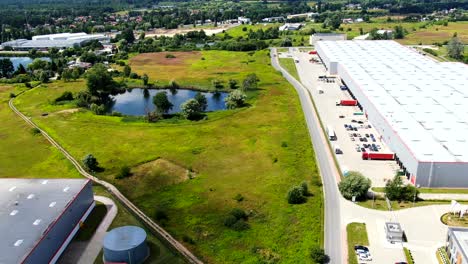 Aerial-Shot-of-Truck-with-Attached-Semi-Trailer-Leaving-Industrial-Warehouse-Storage-Building-Loading-Area-where-Many-Trucks-Are-Loading-Unloading-Merchandise