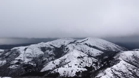 Mountain-range-covered-in-white-snow,-overcast-snowfall,-establisher,-aerial