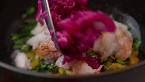 Chef-prepares-cebiche-by-placing-red-onion-and-prawns-in-a-bowl-with-coriander-and-yellow-pepper