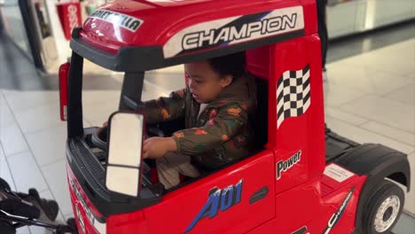 Cute-and-exotic-two-year-old-black-baby,-mix-raced,-riding-a-big-red-toy-truck-inside-a-mall