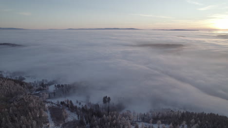 Ein-Panorama-In-Der-Winterlandschaft-Während-Des-Sonnenuntergangs-Mit-Dichtem-Nebel,-Der-Die-Landschaft-Und-Den-Hügel-Bedeckt