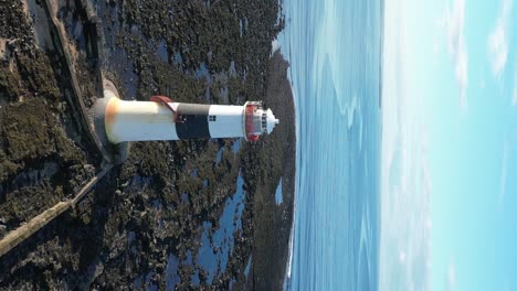 Coastal-Lighthouse-on-barren-island-rock-orbiting-vertical-aerial