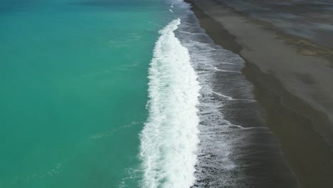 Aerial-slow-motion-over-beautiful-turquoise-colored-South-Pacific-Ocean-as-white-water-contrasts-with-dark-stony-shore---Birdlings-Flat-Beach