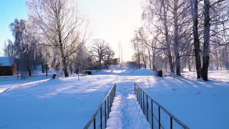Small-bridge-covered-in-snow-leading-to-countryside-farmstead,-tilt-up-view