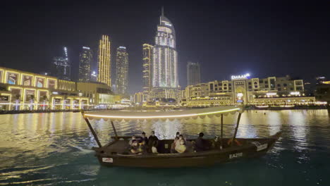 Un-Barco-Lleno-De-Gente-Visitando-La-Fuente-De-Dubai-Por-La-Noche,-Entre-Los-Espectáculos-Acuáticos,-Cerca-De-Lujosos-Restaurantes-Y-Hoteles