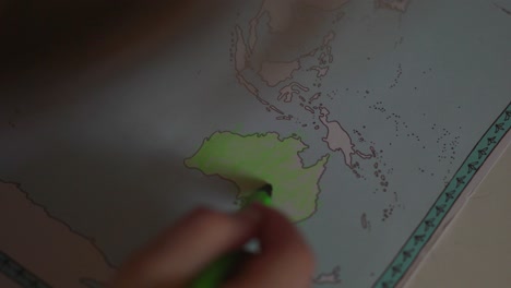 A-toddler-girl-is-coloring-the-continent-of-Australia-with-a-green-pencil-in-a-World-Atlas-educational-book