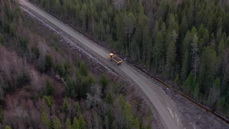Articulated-truck-driving-through-a-dirt-road-in-the-middle-of-the-forest-with-cargo-from-a-construction-site,-heavy-equipment
