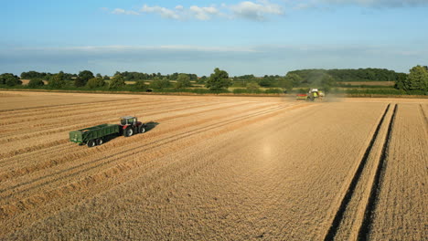 Low-Drone-Shot-of-Claas-Combine-Harvester-at-End-of-Field-and-Turning-Left-with-Tractor-and-Trailer-in-the-Foreground