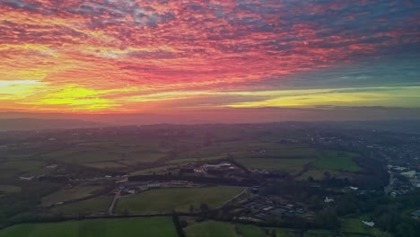 Panning-Drone-Cinematic-Countryside-Scenery-Green-Misty-Fields-Colorful-Red-Sunset-Horizon-Fiery-Clouds