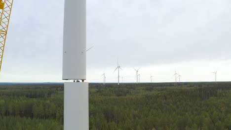 Group-of-workers-assembling-the-parts-of-a-wind-turbine-mast-during-construction-with-a-crane,-drone-shot