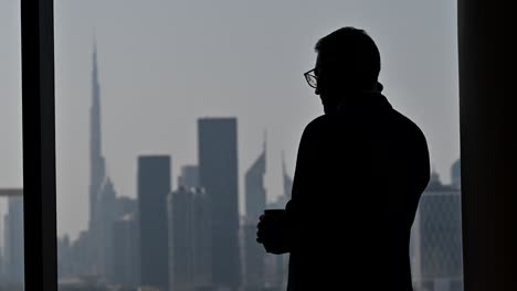 4k:-Silhouette-Eines-Geschäftsmannes,-Der-Am-Fenster-Telefoniert,-Das-Höchste-Gebäude-Der-Welt-„Burj-Khalifa“-Im-Hintergrund