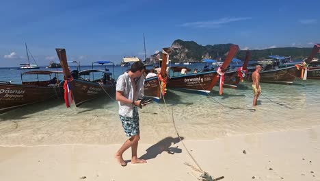 POV-Zu-Fuß-An-Einer-Reihe-Traditioneller-Longtail-Boote-Am-Strand-In-Phi-Phi,-Thailand-Vorbei