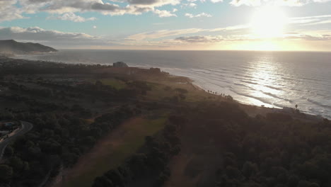 Drone-shot-over-green-golf-coarse-by-coast-side-in-golden-hour
