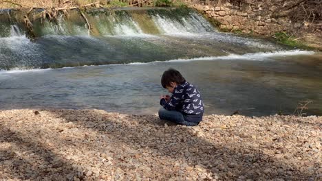 boy-playing-with-stones-on-the-river-bank