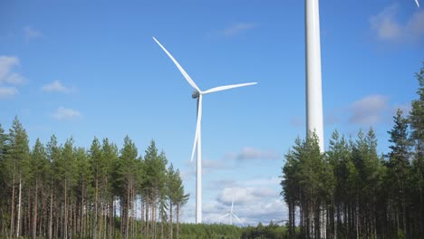 Low-angle-panning-shot,-wind-turbines-on-a-wind-farm-in-the-middle-of-the-woods,-renewable-energy-concept