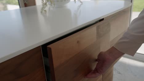 Woman-opens-cutlery-drawer-wooden-cabinet-with-white-worktop
