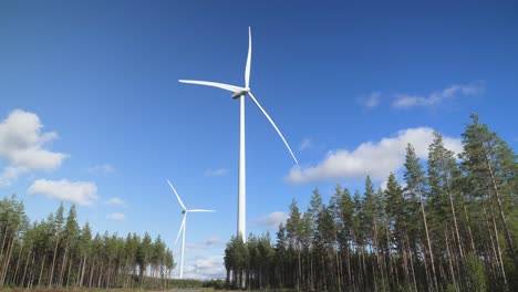 Low-angle-shot-of-two-wind-turbines-in-the-middle-of-a-woodland-during-a-sunny-day,-seen-from-below