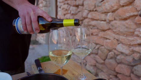 Serving-Spanish-white-wine-in-two-glasses-with-a-Mediterranean-style-stone-wall-in-the-background