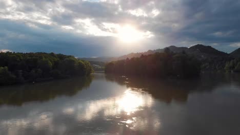 Fast-flight-towards-epic-sunset-with-sunrays-over-river-Drau-near-Maribor-Slowenia-with-forests-in-the-background