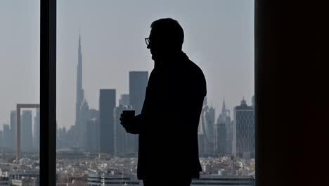 4k:-Silhouette-Eines-Geschäftsmannes,-Der-Am-Fenster-Telefoniert,-Das-Höchste-Gebäude-Der-Welt-„Burj-Khalifa“-Im-Hintergrund
