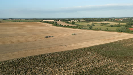 Wide-Angle-Establishing-Drone-Shot-of-Claas-Combine-Harvester-and-Tractor-Working-in-Field-at-Golden-Hour-Evening-UK