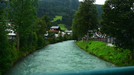 Blue-Glacial-River-Flowing-Through-the-Green-Landscape-of-Kaprun,-Austria-in-Slow-Motion