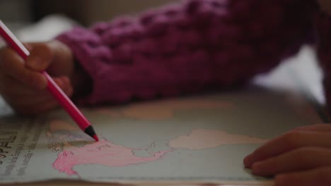 A-toddler-girl-is-coloring-the-continent-of-North-America-with-a-pink-pencil-in-a-World-Atlas-educational-book