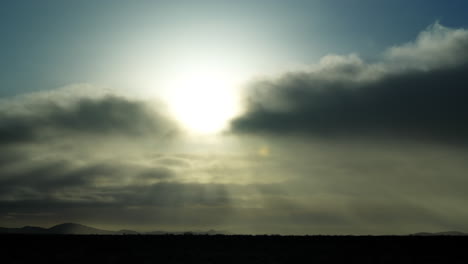 Sunshine-streaming-through-the-clouds-above-the-silhouette-of-the-Mojave-Desert---time-lapse