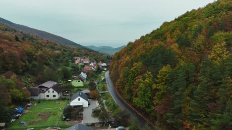 Schönes-Tal-Mit-Dorf,-Herbstbäumen,-Bach-Und-Leerer-Bergstraße-Zwischen-Den-Bäumen