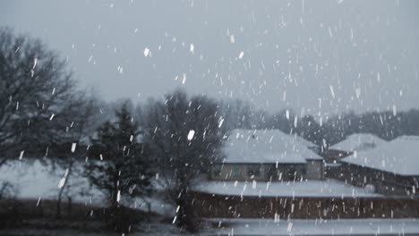 Schnee-Fällt-In-Zeitlupe,-Kamera-Zoomt-Heraus-Mit-Bäumen-Und-Häusern-Im-Hintergrund