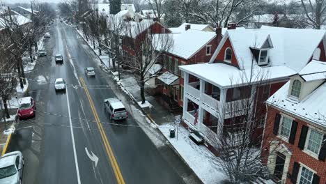 Descending-aerial-of-home-on-snowy-main-street-in-small-town-America-with-American-flag-waving