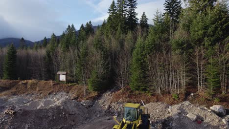 Flying-over-a-bulldozer-in-a-construction-site-showing-beautiful-untouched-forest-and-mountain