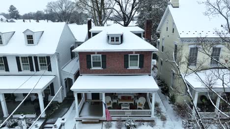 Rising-aerial-of-snow-covered-home-with-American-flag-waving-on-front-porch
