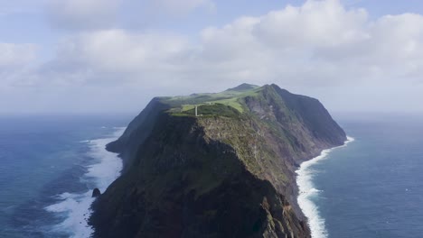 Pull-back-drone-footage-of-a-Lighthouse-on-top-of-dramatic-cliffs-and-the-Atlantic-Ocean-and-the-São-Jorge-island-shape,-in-the-Azores,-Portugal