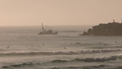 Morning-surf-at-Duranbah-Beach-as-a-fishing-trawler-returns-from-the-pen-ocean,-on-the-Southern-Gold-Coast,-Australia,-in-slow-motion