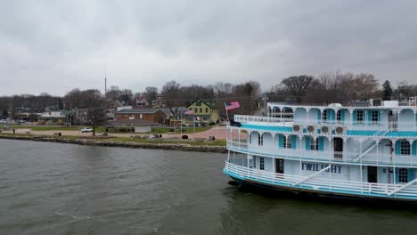 A-close-fly-by-of-a-paddle-steamer-at-dock-in-LeClaire,-Iowa-at-the-beginning-of-winter