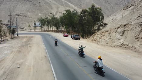 Three-motorcyclists-riding-downhill-a-mountain-road-through-desert-mountains