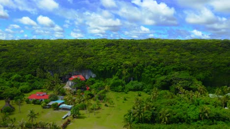 A-drone-captures-a-shot-going-over-a-tropical-beach,-showcasing-the-crystal-clear-waters,-sandy-beaches-and-houses-on-the-shore,-and-then-revealing-the-huge,lush,-verdant-forest-behind-during-the-day