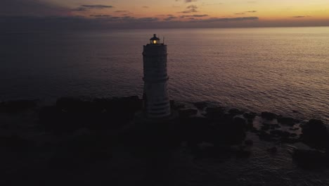 Aerial-drone-flying-towards-offshore-Lighthouse-on-rocks-in-Calasetta,-dusk