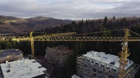 Aerial-view-of-cranes-in-a-construction-site-on-a-mountain-covered-with-forest