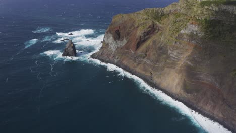 Top-down-drone-footage-of-waves-crashing-on-dramatic-cliffs-revealing-a-lighthouse-over-the-Atlantic-Ocean-in-Sao-Jorge-island,-Azores,-Portugal