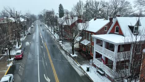 Rising-aerial-shot-of-American-flag-waving-from-front-porch-of-house-on-main-street-of-snowy-small-town-in-America