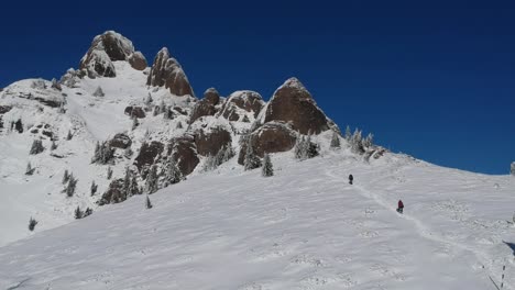 Dron-shot-with-two-persons-slowly-climbing-a-mountain-during-winter-season