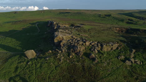 Establishing-Drone-Shot-Flying-Over-the-Cow-and-Calf-Rock-Formation-with-People-Sat-on-Rocks-on-Ilkley-Moor-at-Golden-Hour-West-Yorkshire-UK