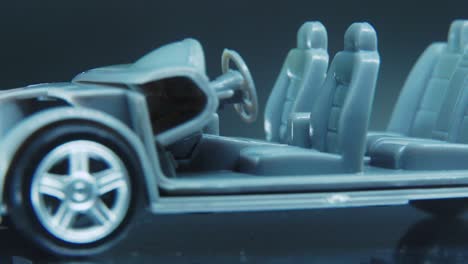 Ein-Winziges-Modell-Metallprobenskelett-Eines-Autos-Auf-Einem-Drehbaren-Ständer-Mit-Studiolichtern,-Makro-Nahaufnahme,-4k-Video,-Silbernen-Rädern,-Schwarzen-Reifen,-Türen-Und-Fenstern,-Kunststoffsitzen