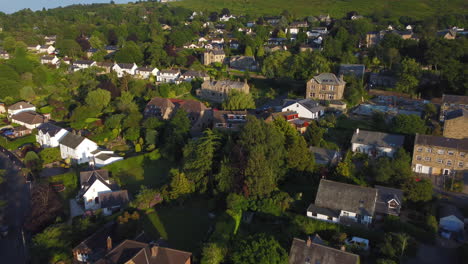 Low-Establishing-Drone-Shot-Over-Houses-Rising-up-to-Reveal-Cow-and-Calf-Rocks-in-Ilkley-Spa-Town-West-Yorkshire-UK-at-Golden-Hour