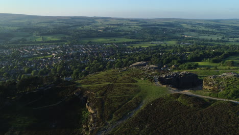 Establishing-Drone-Shot-Over-Back-of-Cow-and-Calf-Rocks-Looking-Over-Valley-with-Ilkley-Spa-Town-on-Sunny-Summer-Day-at-Golden-Hour-West-Yorkshire-UK