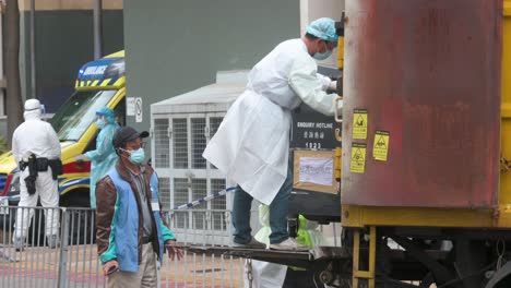 Sanitation-and-health-officials-throw-waste-into-a-garbage-container-outside-a-building-placed-under-lockdown-after-a-large-number-of-residents-tested-Covid-19-Coronavirus-positive